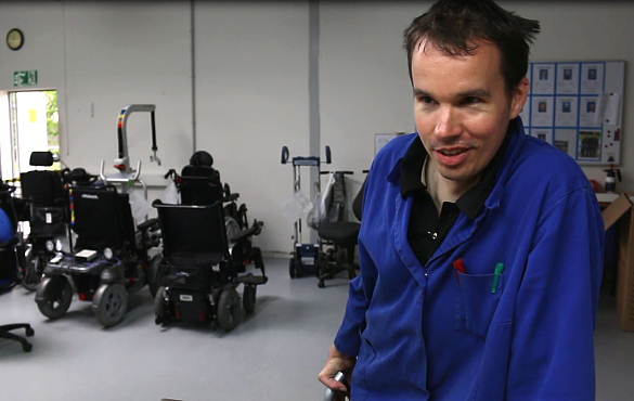 Ein Mann in einem blauen steht in einer Werkstatt, in der Rollstühle repariert werden.