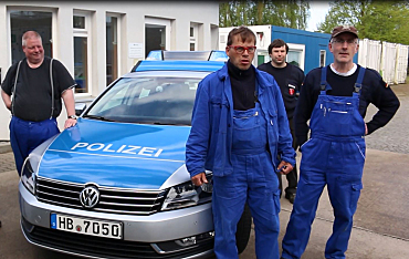 Vier Männer in Arbeitskleidung stehen rund um ein Polizeiauto.