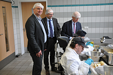 Betriebstätten-Leiter Dirk Dieling, Geschäftsführer Ahlrich Weiberg und Präsident Christian Weber schauen einer Beschäftigten in der Marmeladenproduktion über die Schulter